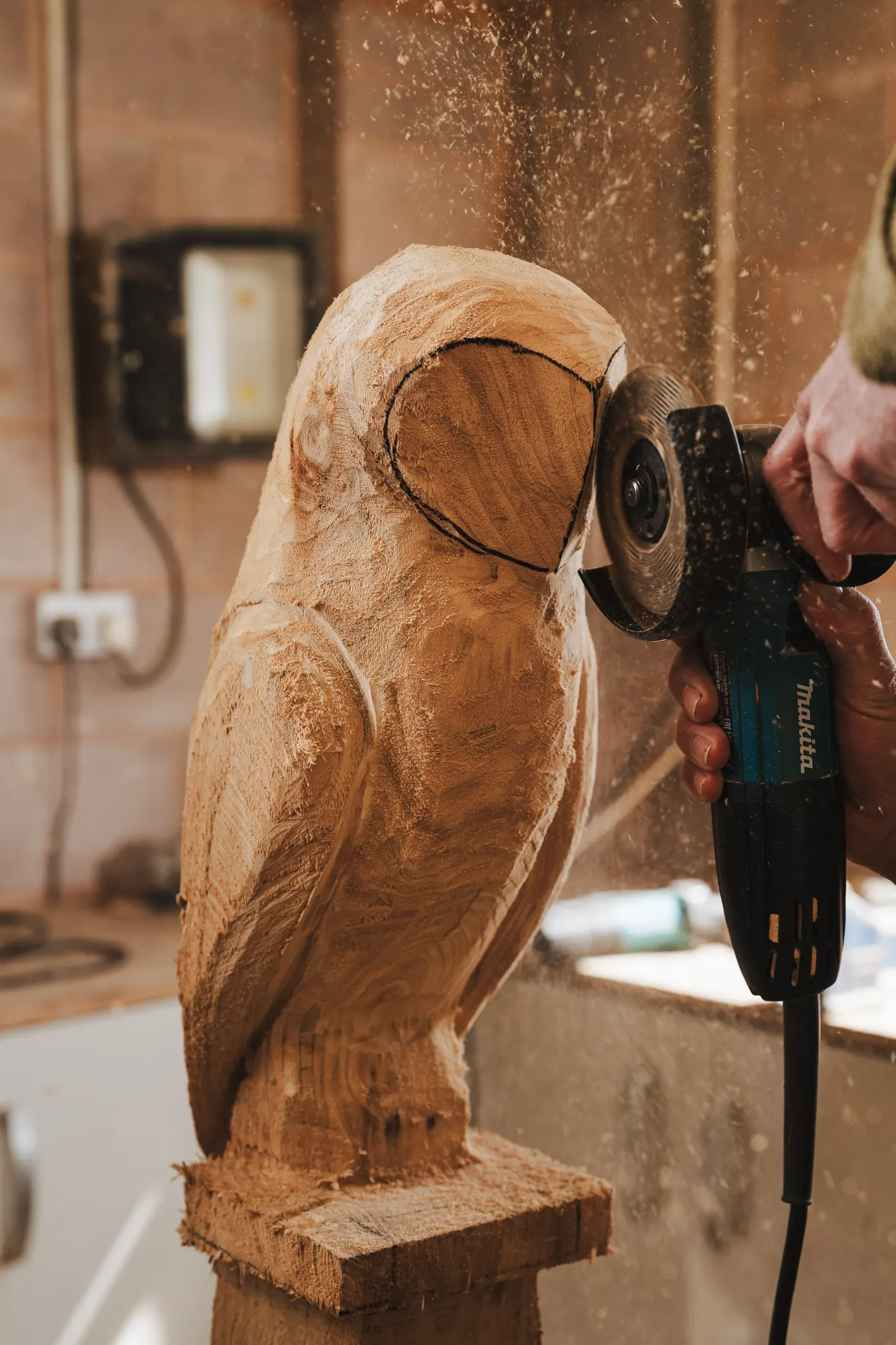 Shaping the head and ear detail of a wooden owl carving with an angle grinder