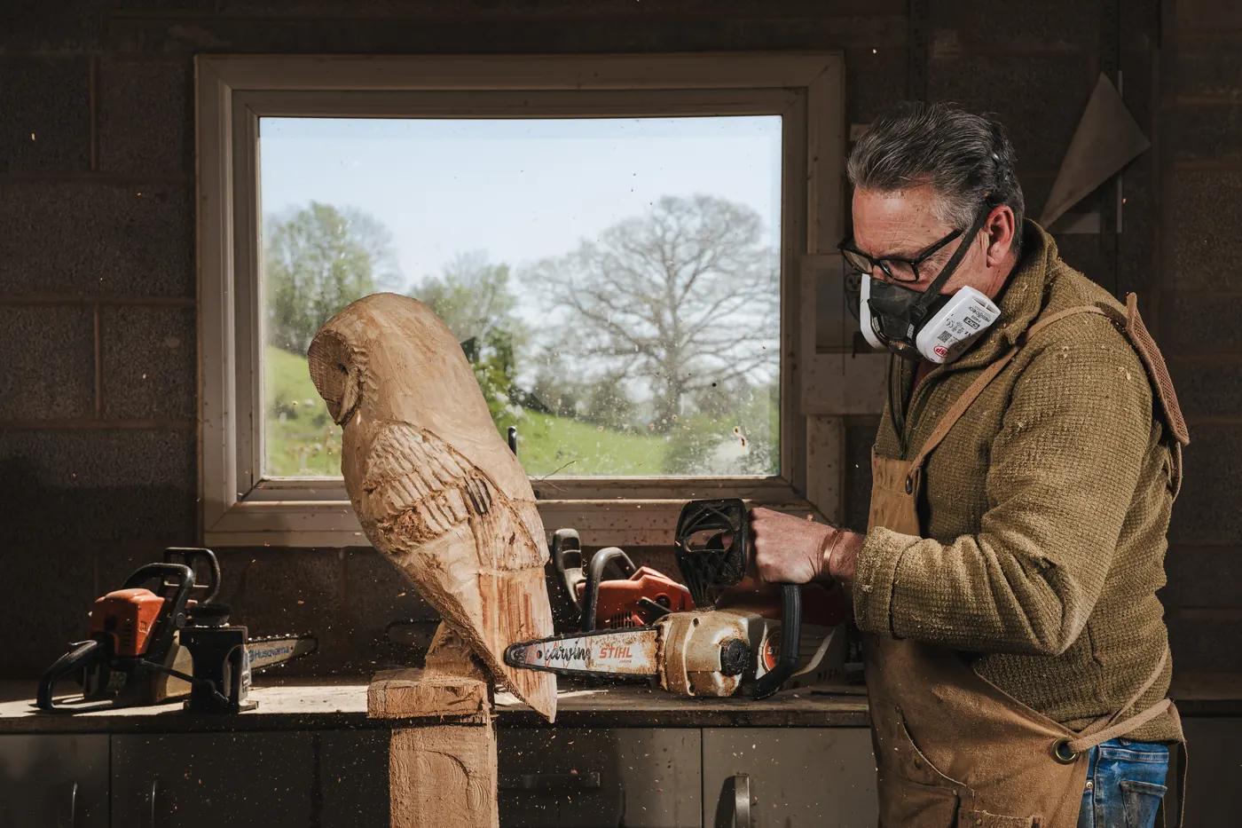 Cutting feather detail into a wooden barn owl's wing with a small carving chainsaw